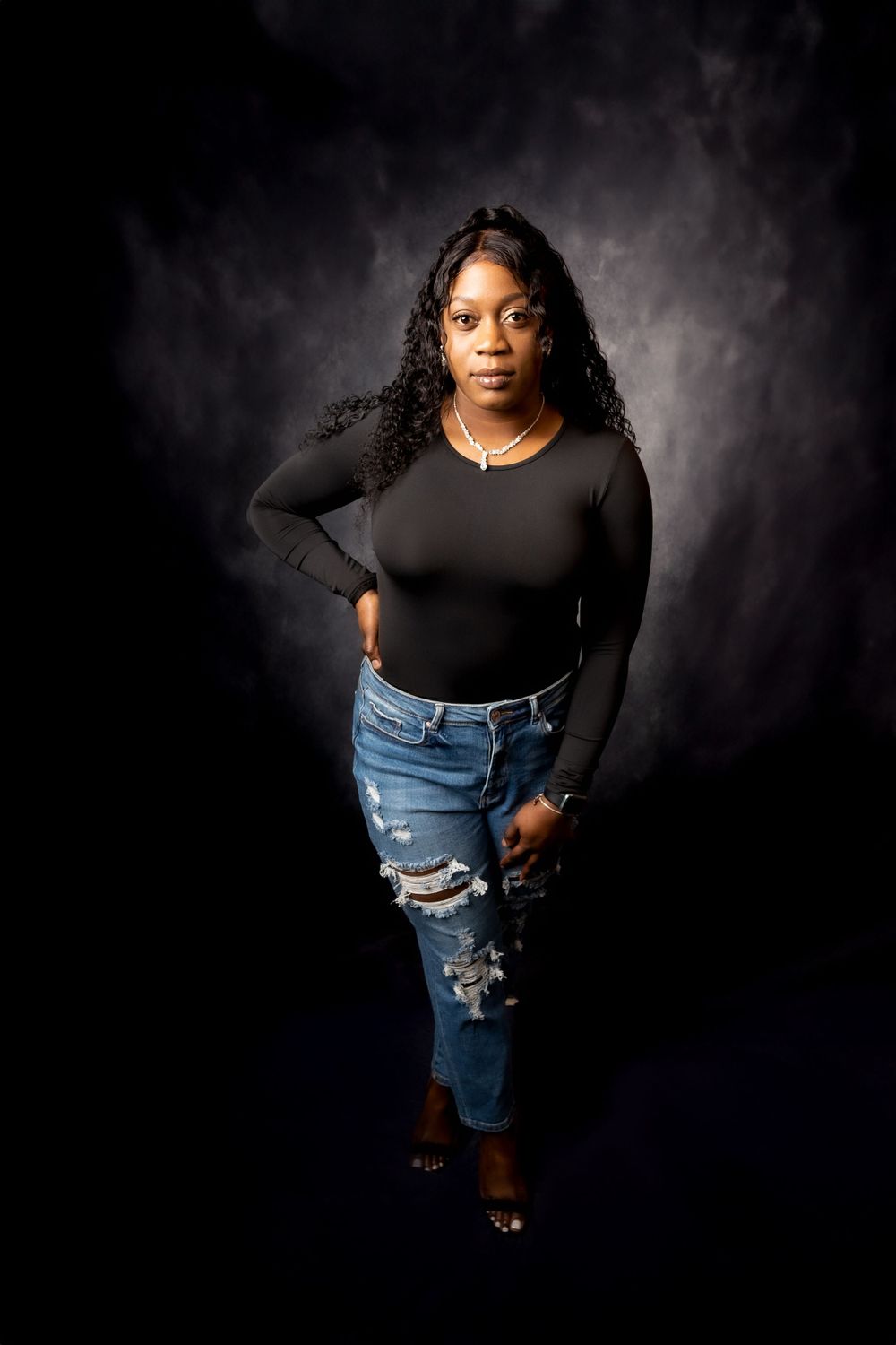 Stylish casual look featuring black top and distressed jeans in dramatic studio lighting.