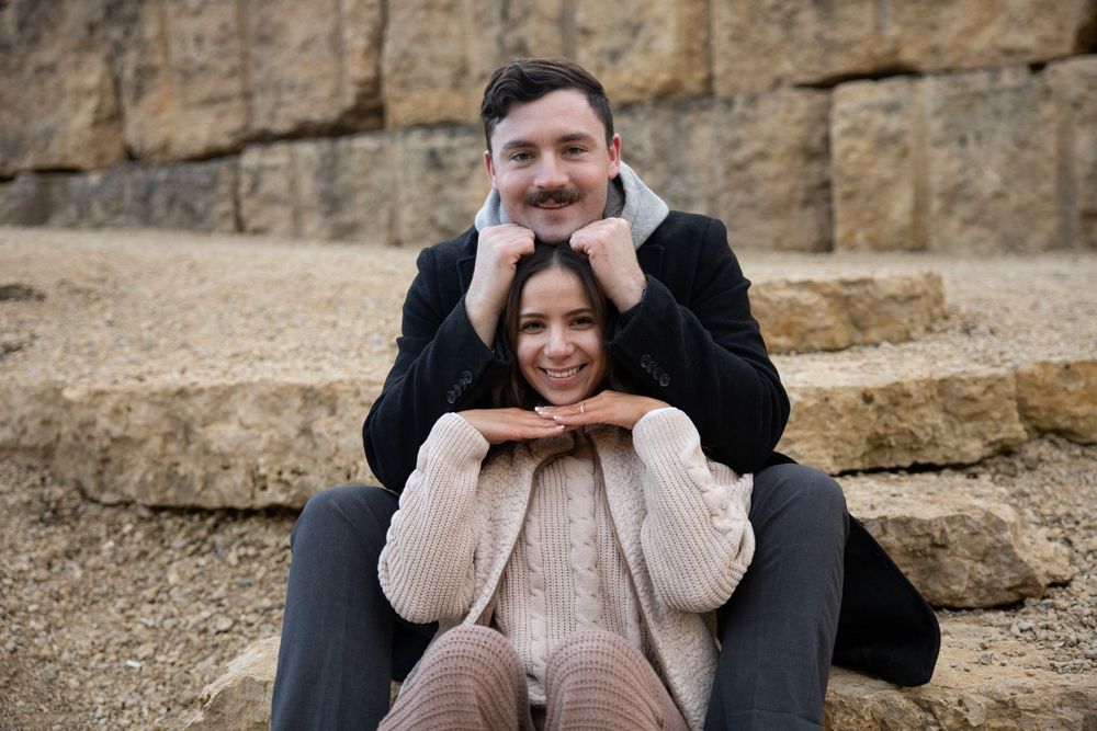 A playful couple poses on stone steps in front of a cliff face.
