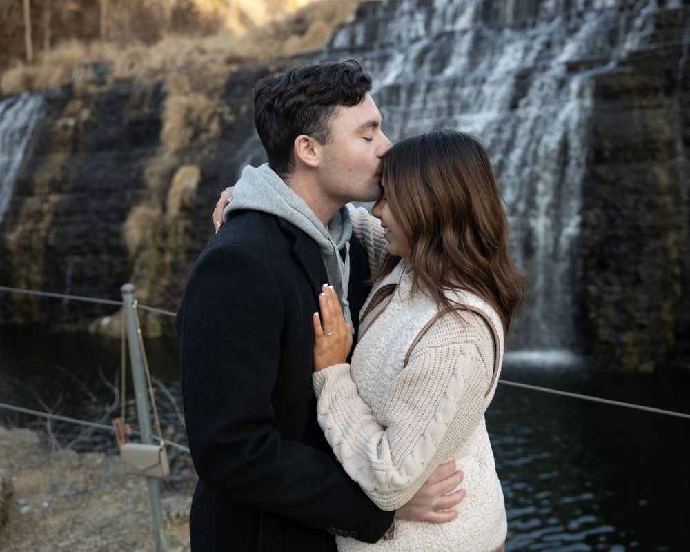 A romantic embrace with a scenic waterfall backdrop at dusk.