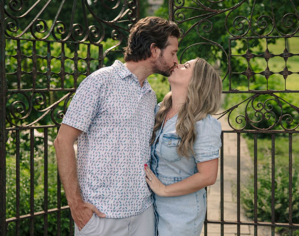 A couple sharing a kiss while standing together by an ornate garden gate.