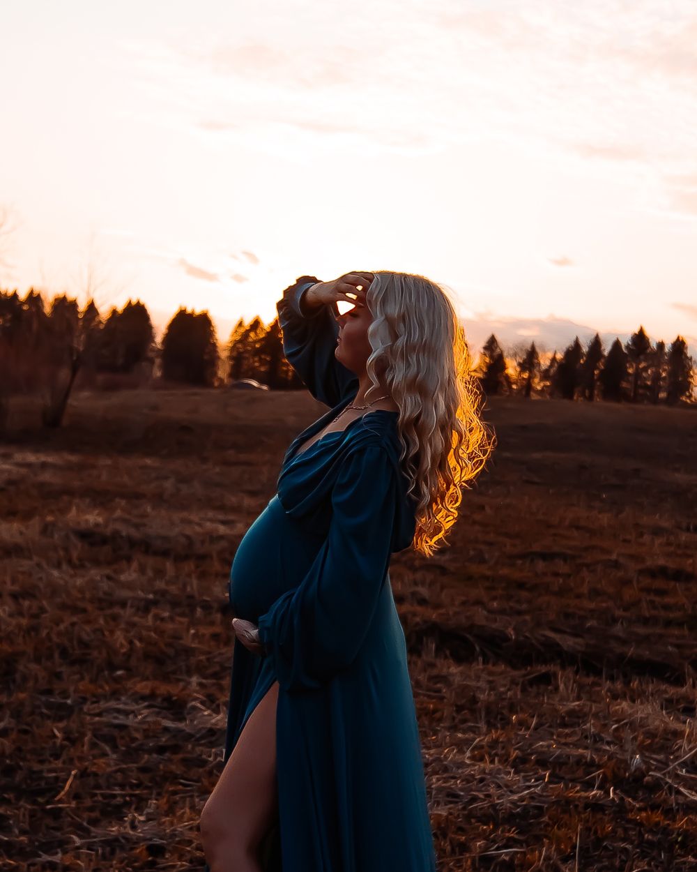 Silhouette of pregnant figure in blue dress against golden sunset.