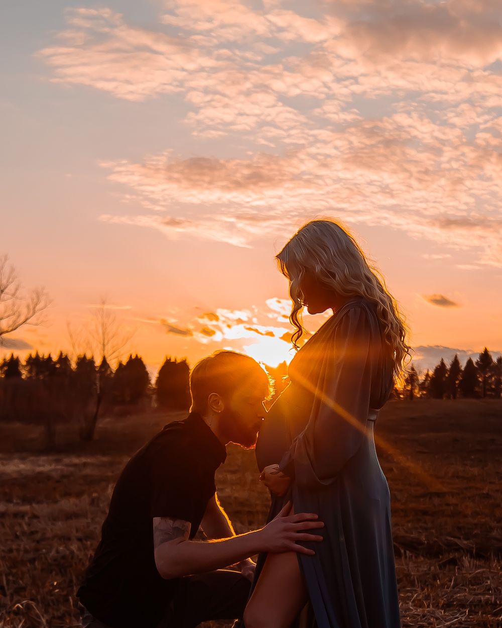Romantic sunset maternity shoot with couple in field.