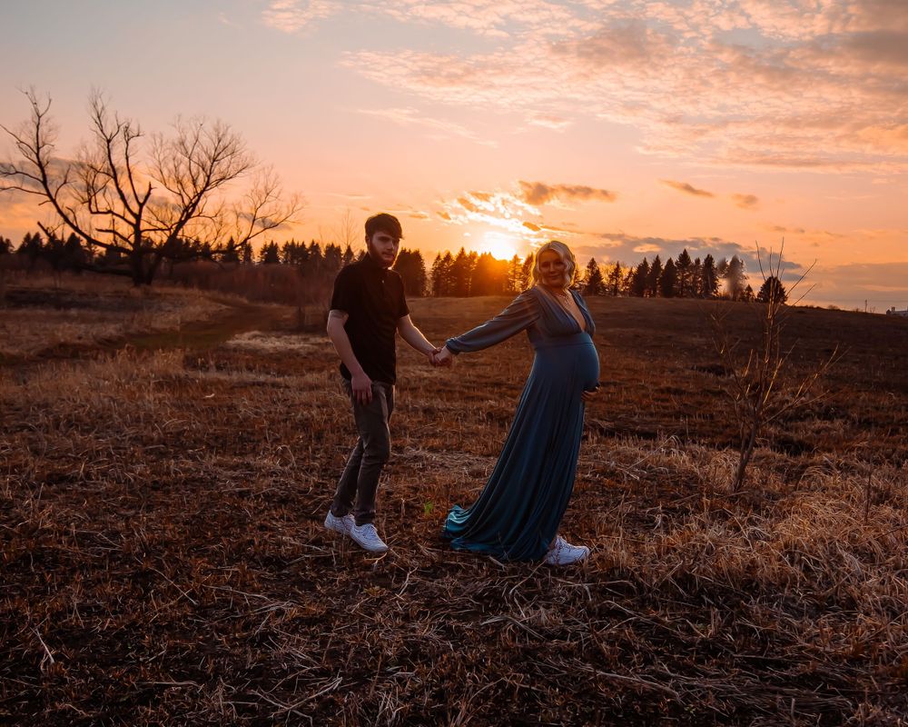 Couple holding hands at sunset in field with trees in background.