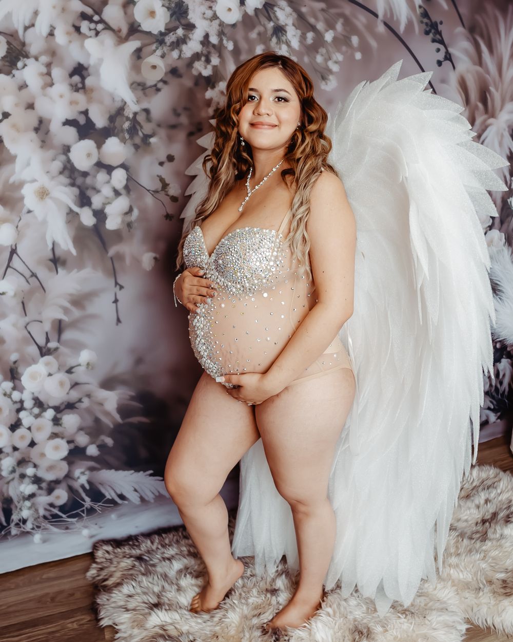 Maternity portrait with white feathered wings and sparkly bodysuit.