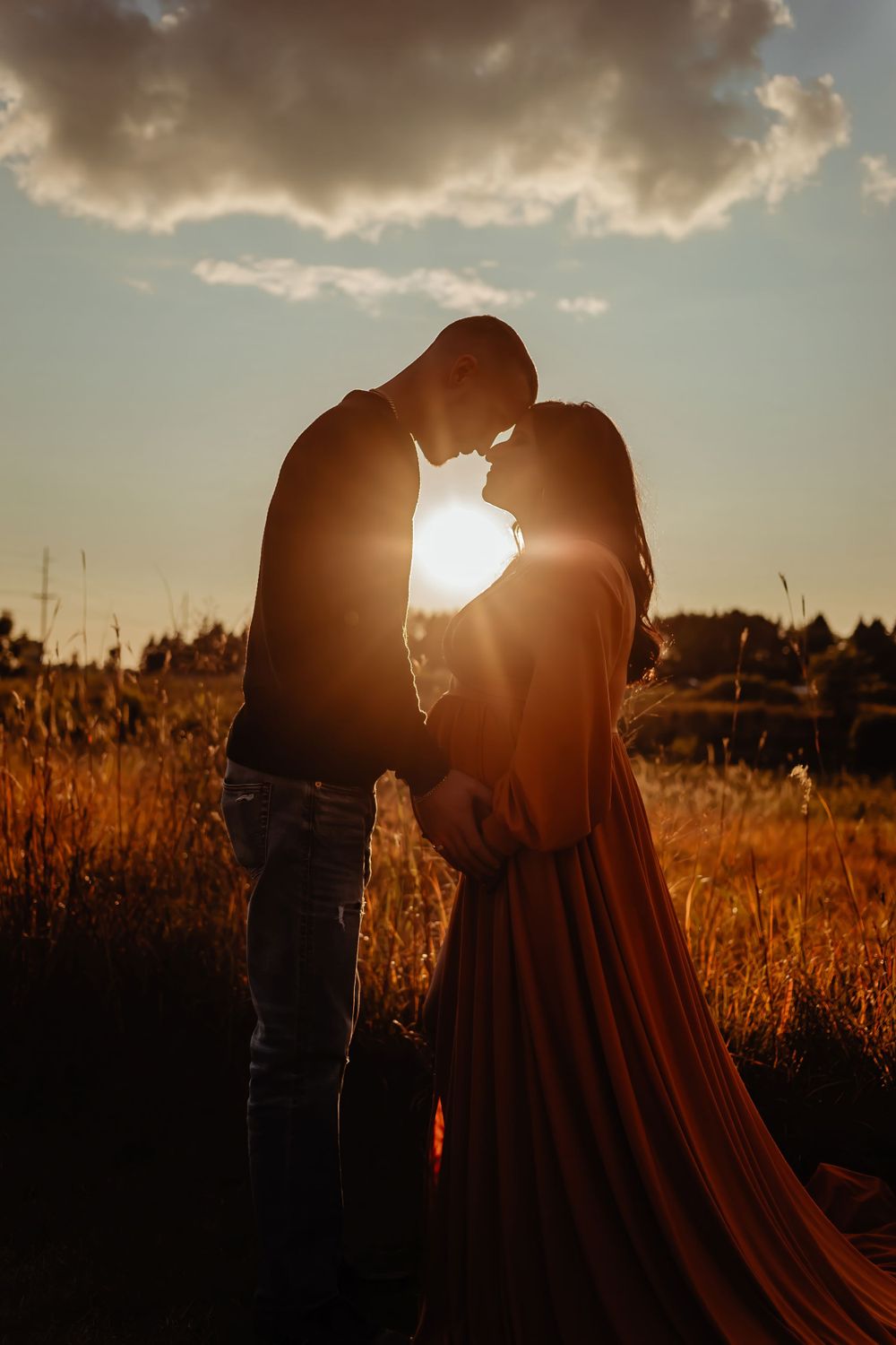 Silhouette of couple embracing in golden sunset light with dramatic clouds.