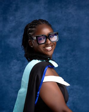 Smiling graduate in black cap and gown with teal hood and bold glasses poses for portrait photo.