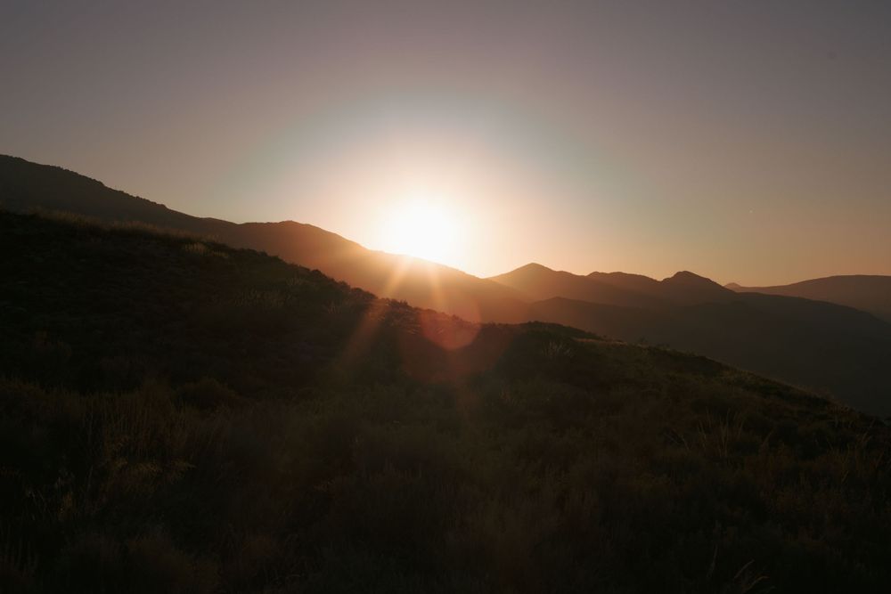 Sun setting behind mountain peaks creating a dramatic silhouette against the sky.
