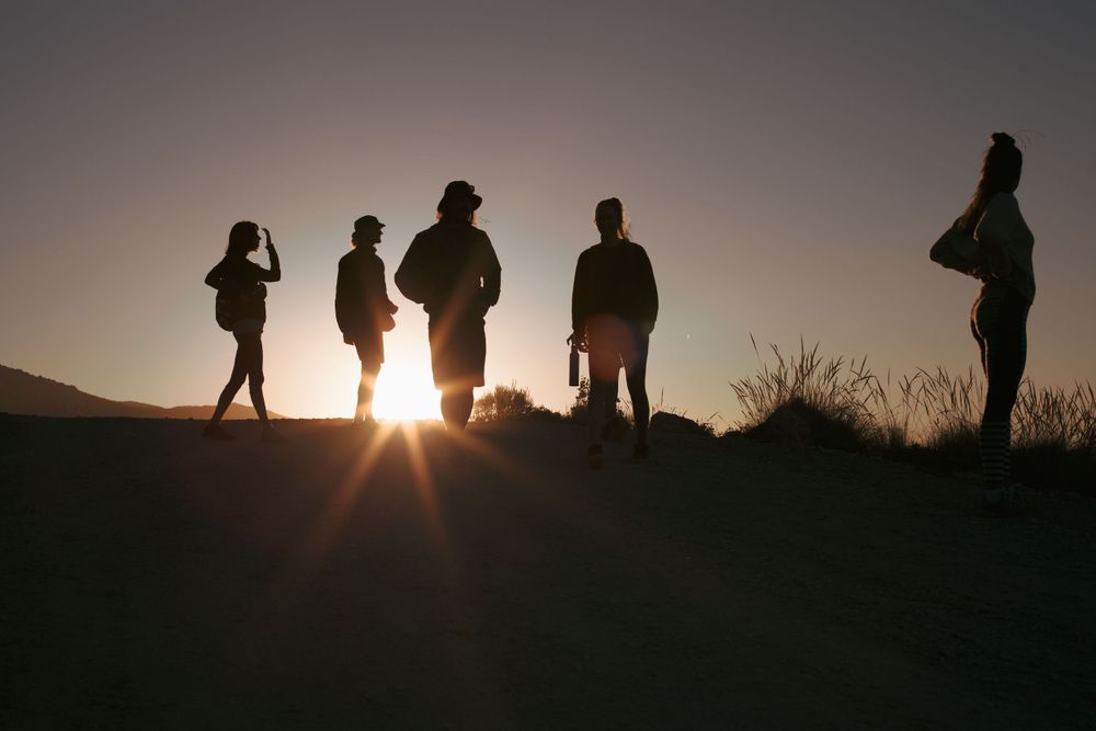Silhouettes of people standing on a hill against a dramatic sunset sky.