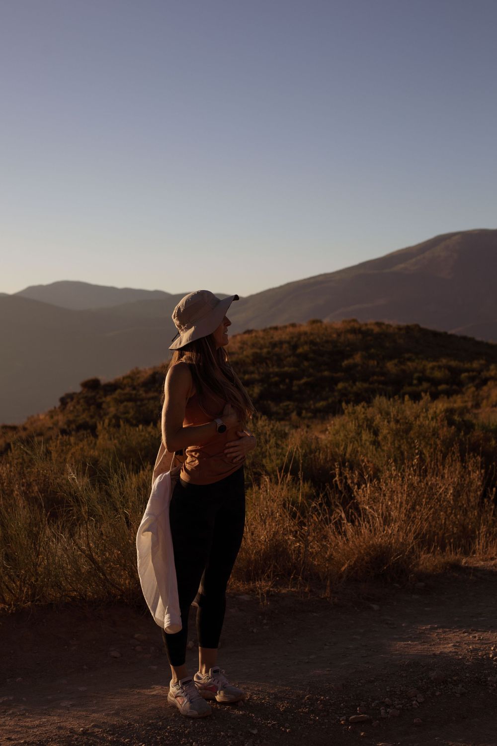 Two figures embracing on a hilltop at sunset with mountains in the background.