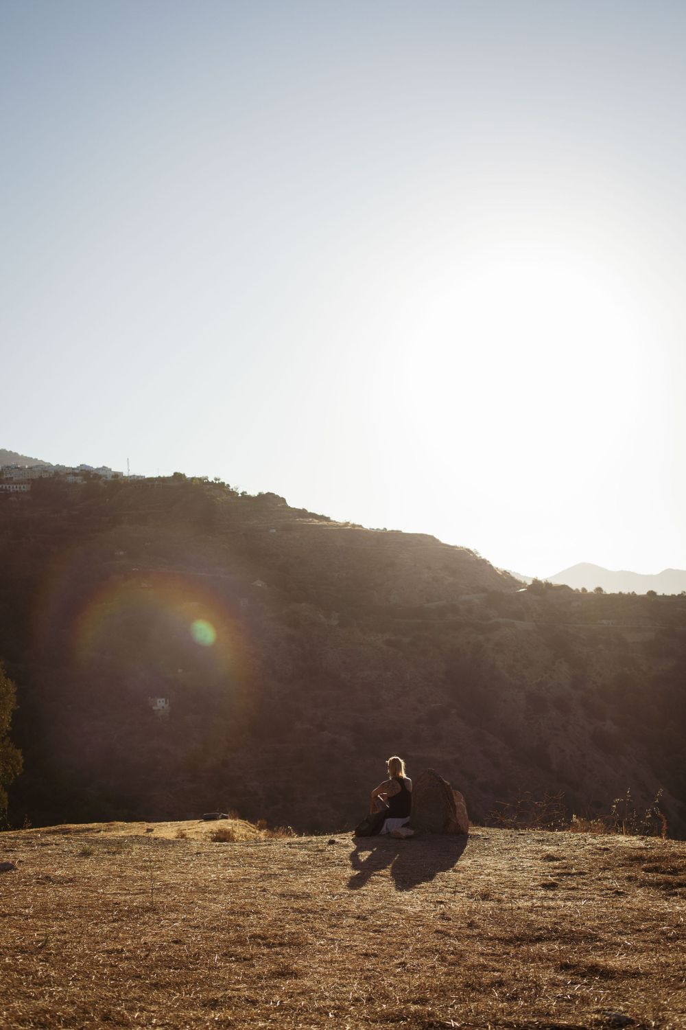 Figure sitting on a hillside during golden hour with mountains in the distance.