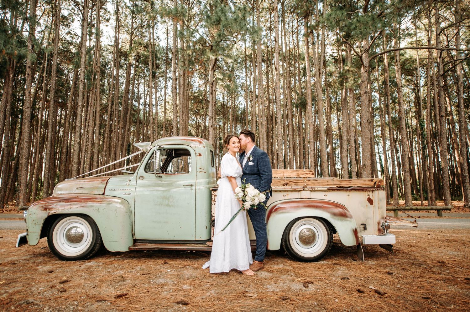 A classic mint green truck serves as backdrop for wedding photos in a pine forest.