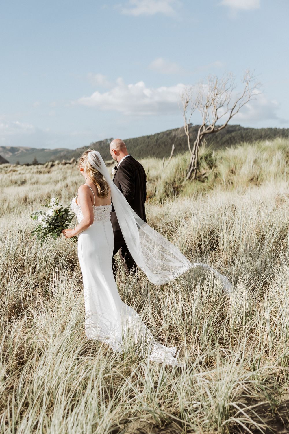 bride and groom walking at Muriwai beach after their wedding at Tui Hill wedding venue. AUckland Wedding Photographer