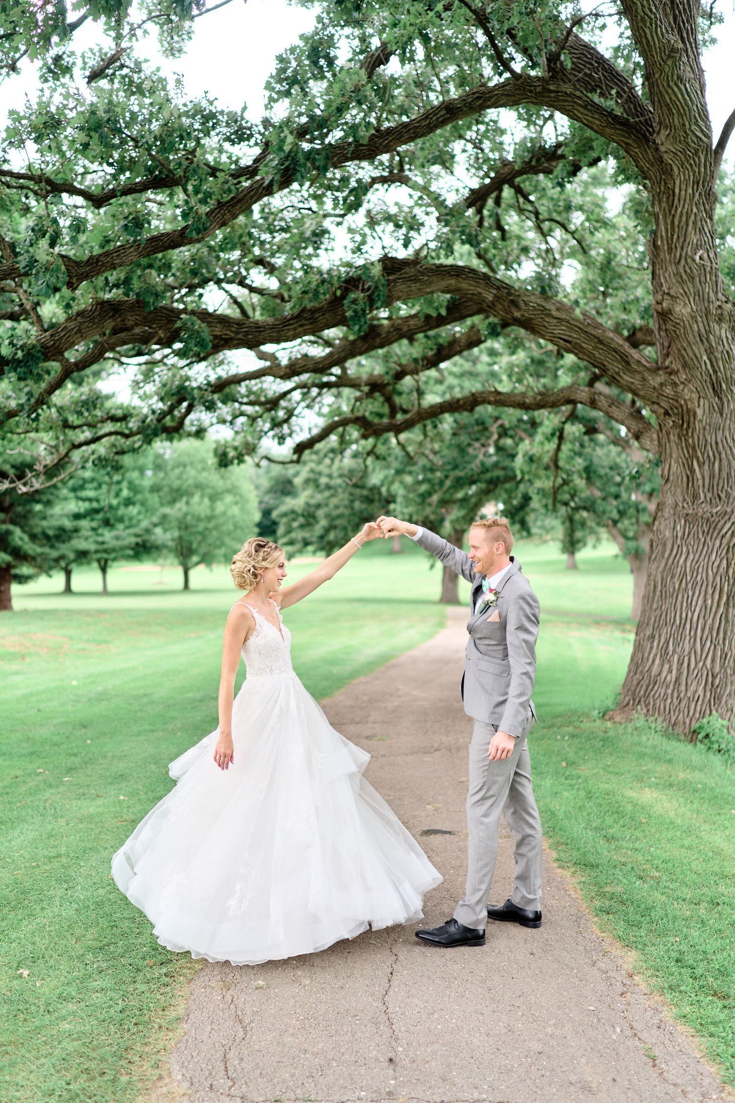 A couple shares a romantic moment dancing on a path under a large oak tree during their wedding day.