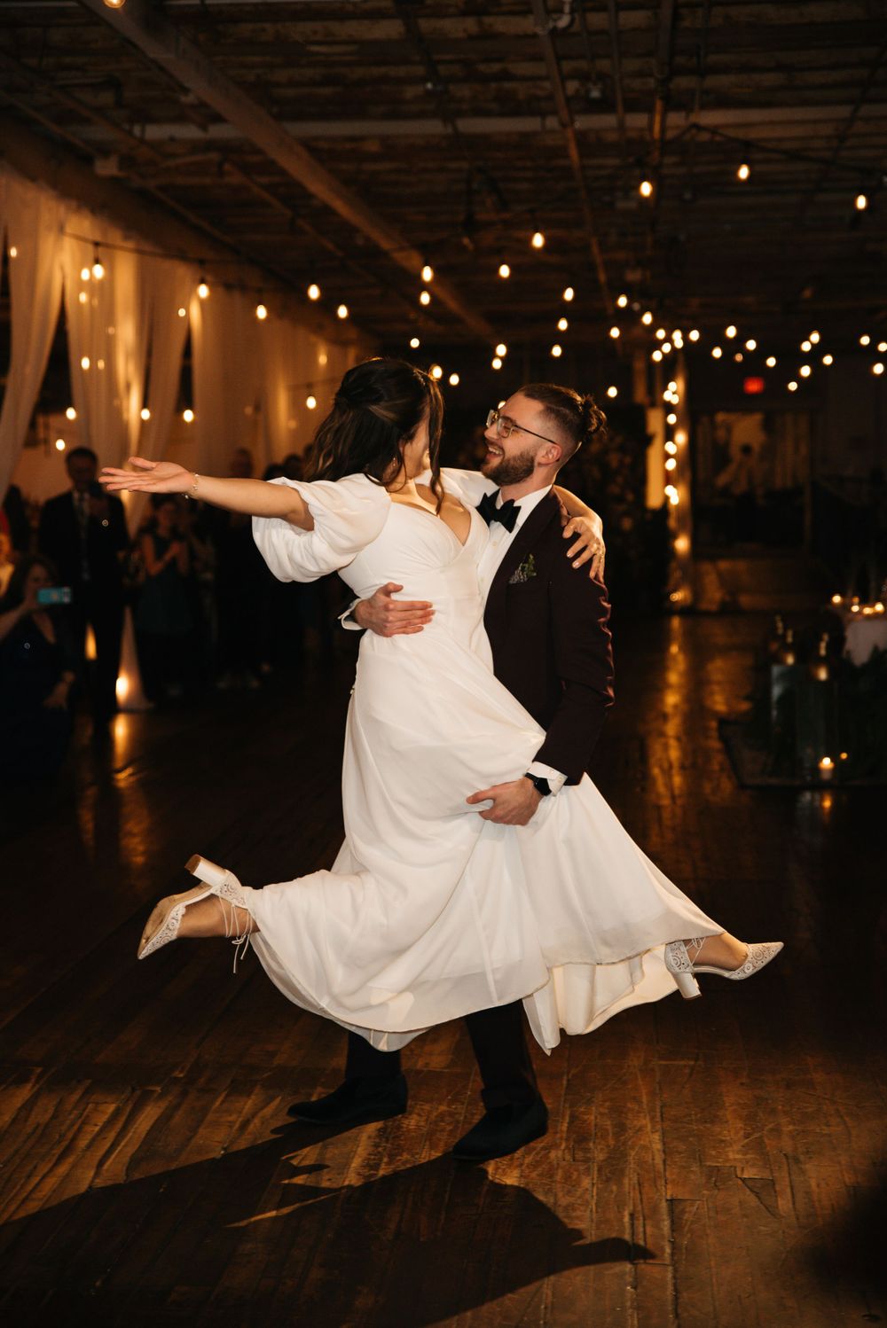 Romantic first dance at wedding reception with twirling bride in flowing white dress.