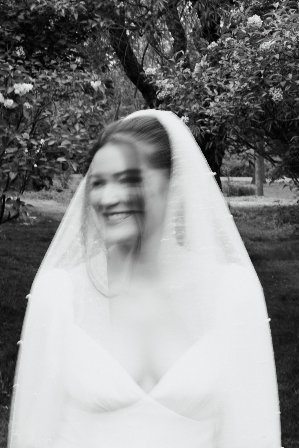 Black and white motion portrait of a bride laughing under her veil.