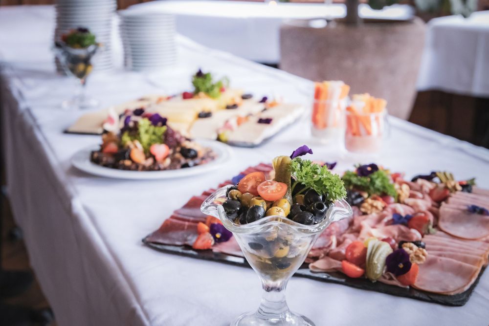Elegant gedeckter Tisch mit Vorspeisentellern mit Sushi, Charcuterie und Meeresfrüchten auf weißem Tischtuch.