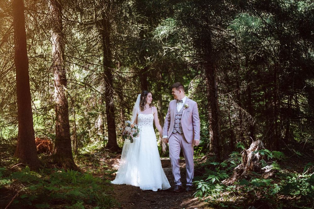 Bride and groom holding hands walking through a sunlit forest on their wedding day.