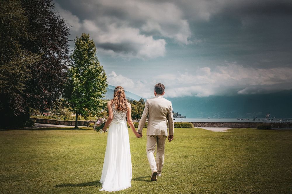 Couple holding hands while walking on grass with dramatic sky background.