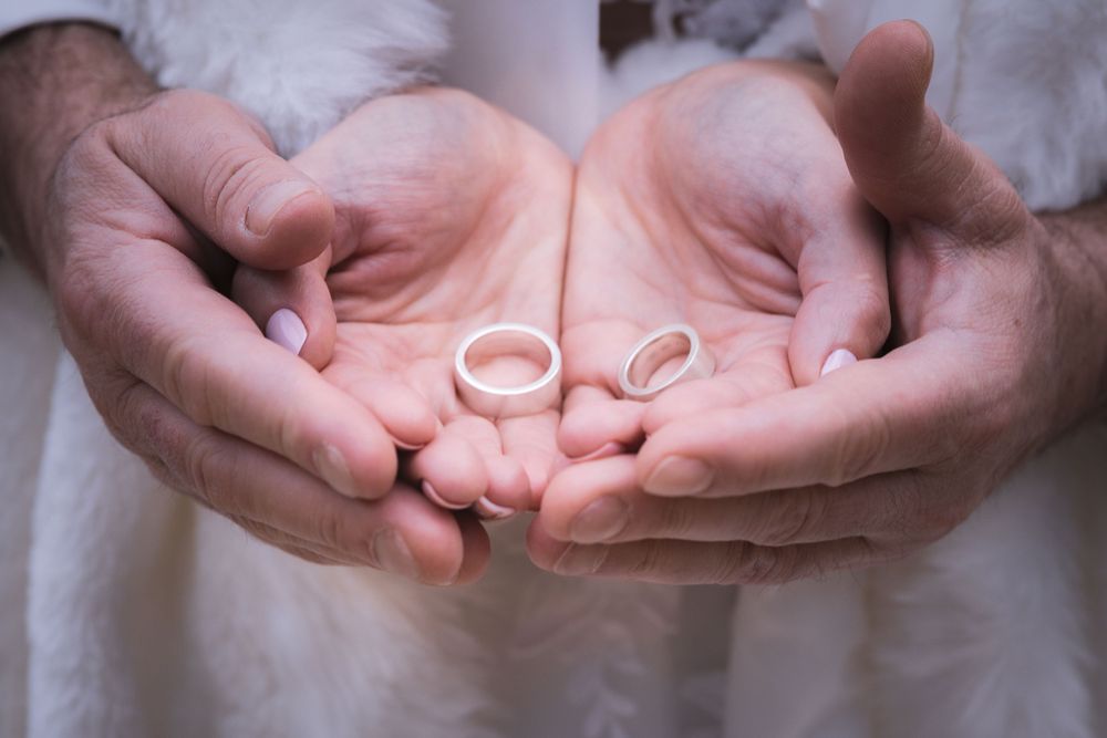 Two silver wedding rings displayed in open palms with white fabric background.