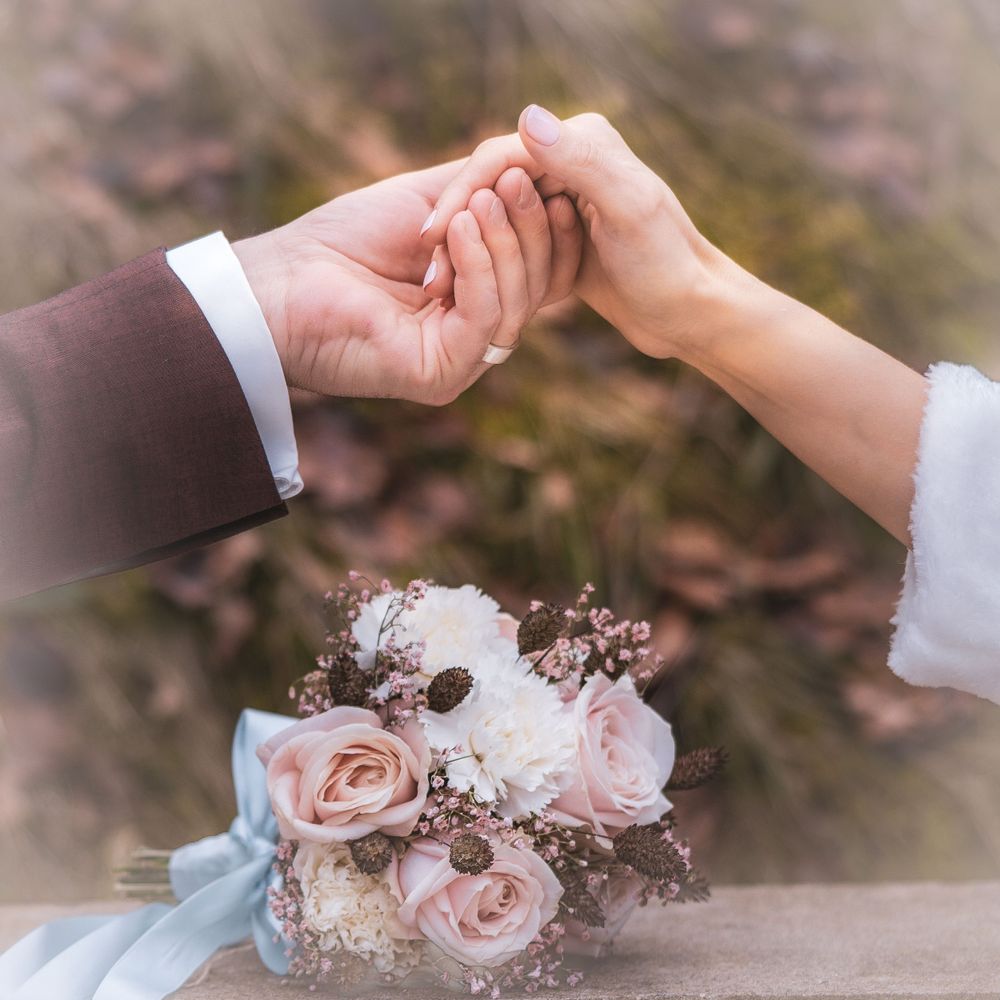 Couple holding hands with romantic pink floral bouquet in soft focus.