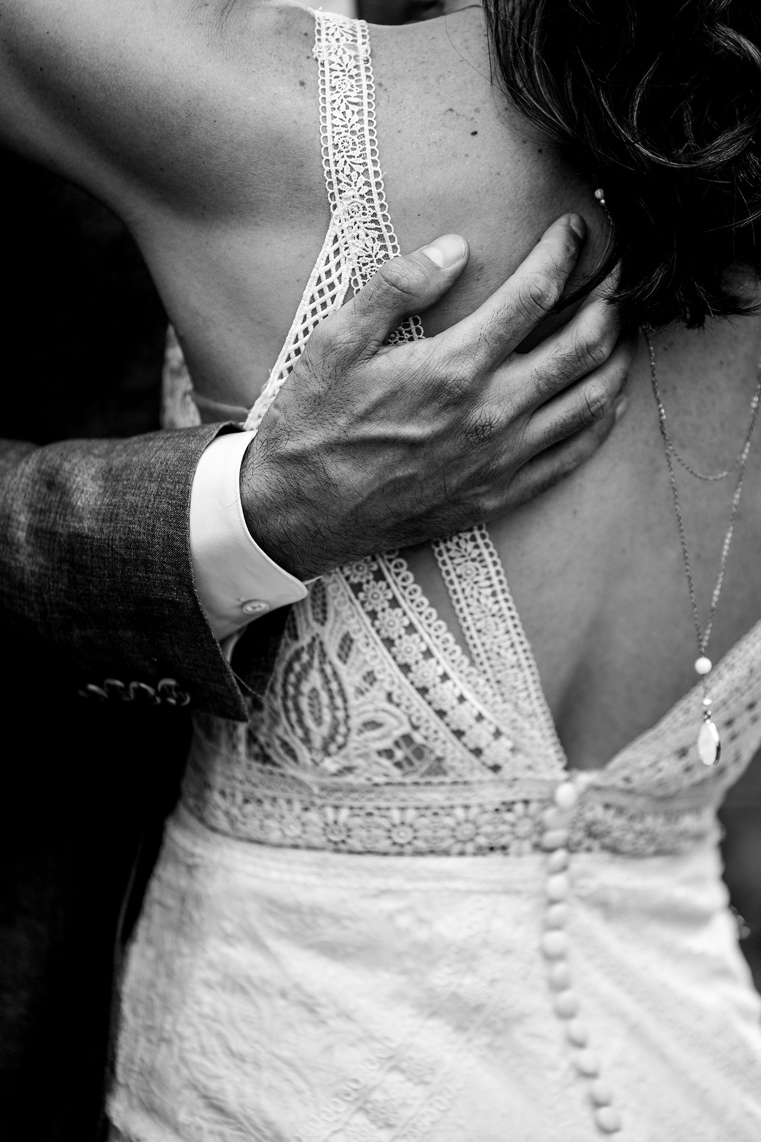Close-up of intricate lace detail on back of wedding dress with gentle hand placement.