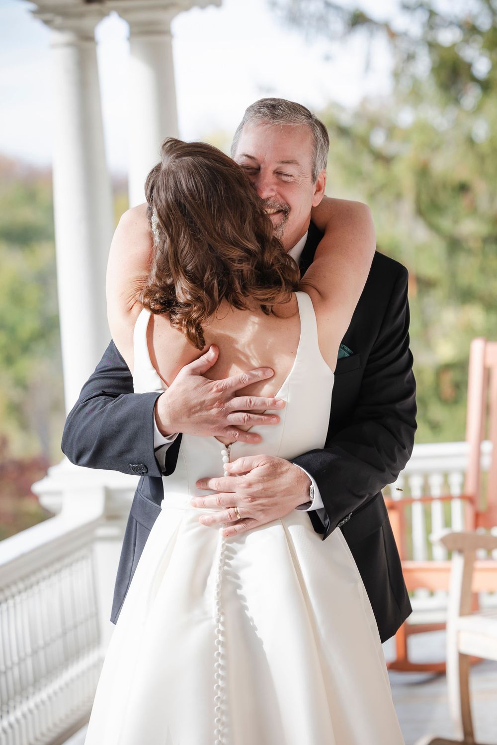 A tender embrace between a bride and her father on the wedding day on an elegant porch with white columns.