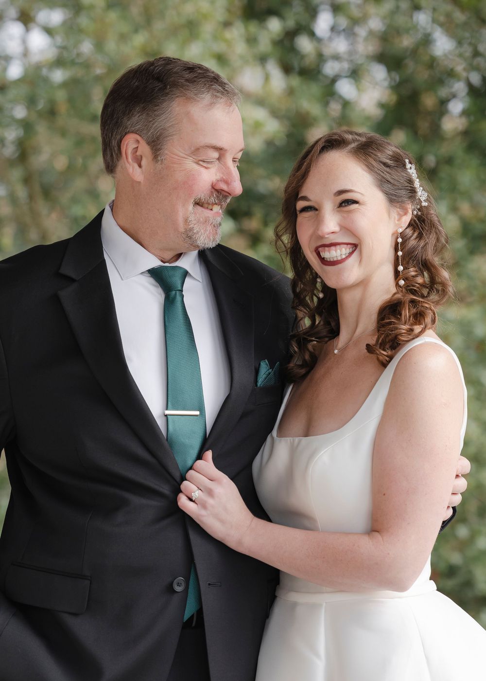 A close-up portrait of a joyful bride and her dad dressed in formal attire sharing a tender moment outdoors.