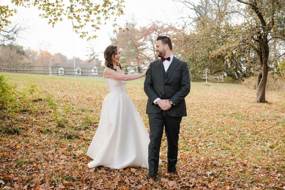 A bride and groom share a first look in a rustic autumn setting with yellow leaves and a house in the background.