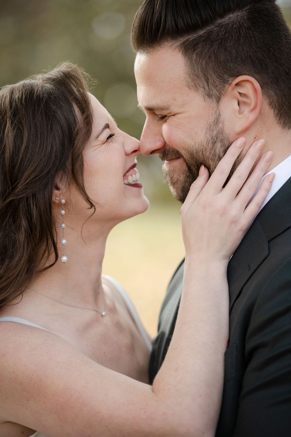 A joyful romantic moment between newlyweds sharing an intimate close-up smile outdoors on their wedding day.