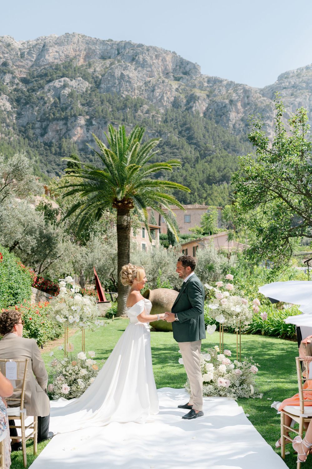 An outdoor wedding ceremony set in a lush garden with mountain backdrop and palm trees in Mallorca, Spain.