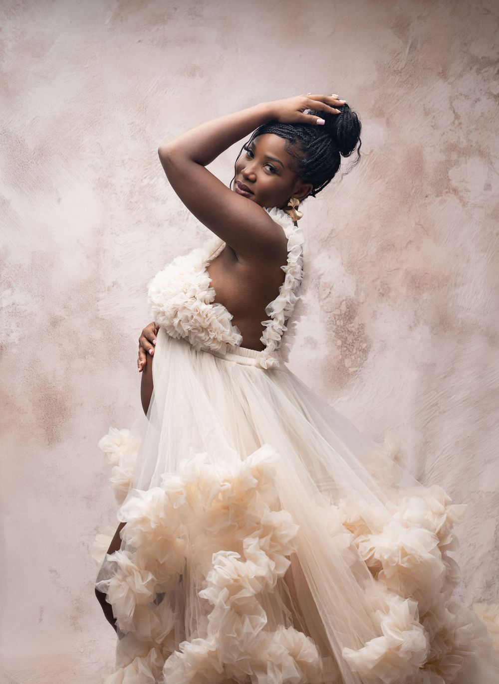 A stunning portrait in soft beige tones featuring an elegant flowing dress with dramatic tulle and ethereal fabric details.