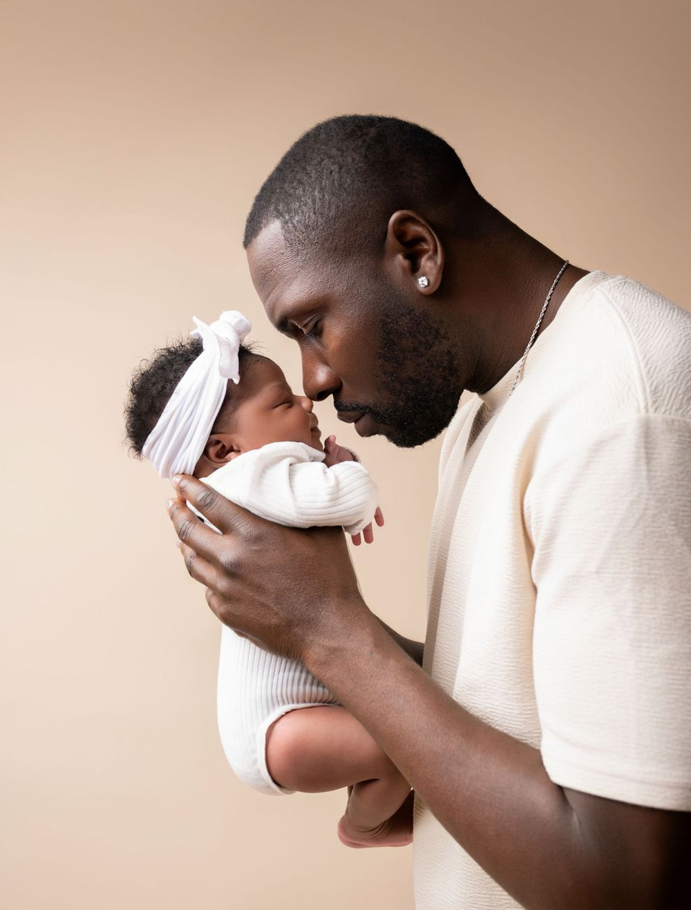A tender moment between parent and infant wearing a white headband against a neutral beige background.
