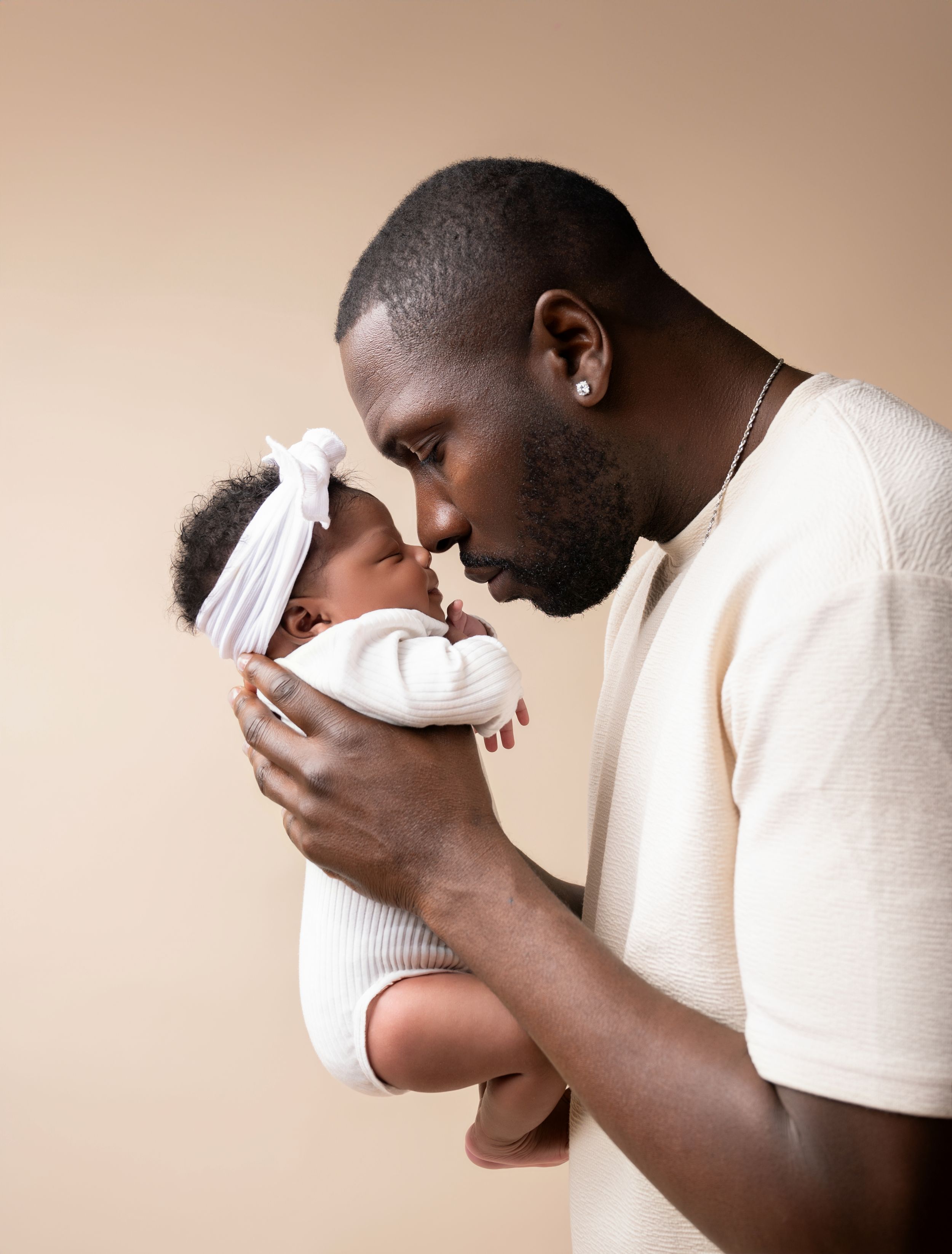 A tender moment between parent and infant wearing a white headband against a neutral beige background.