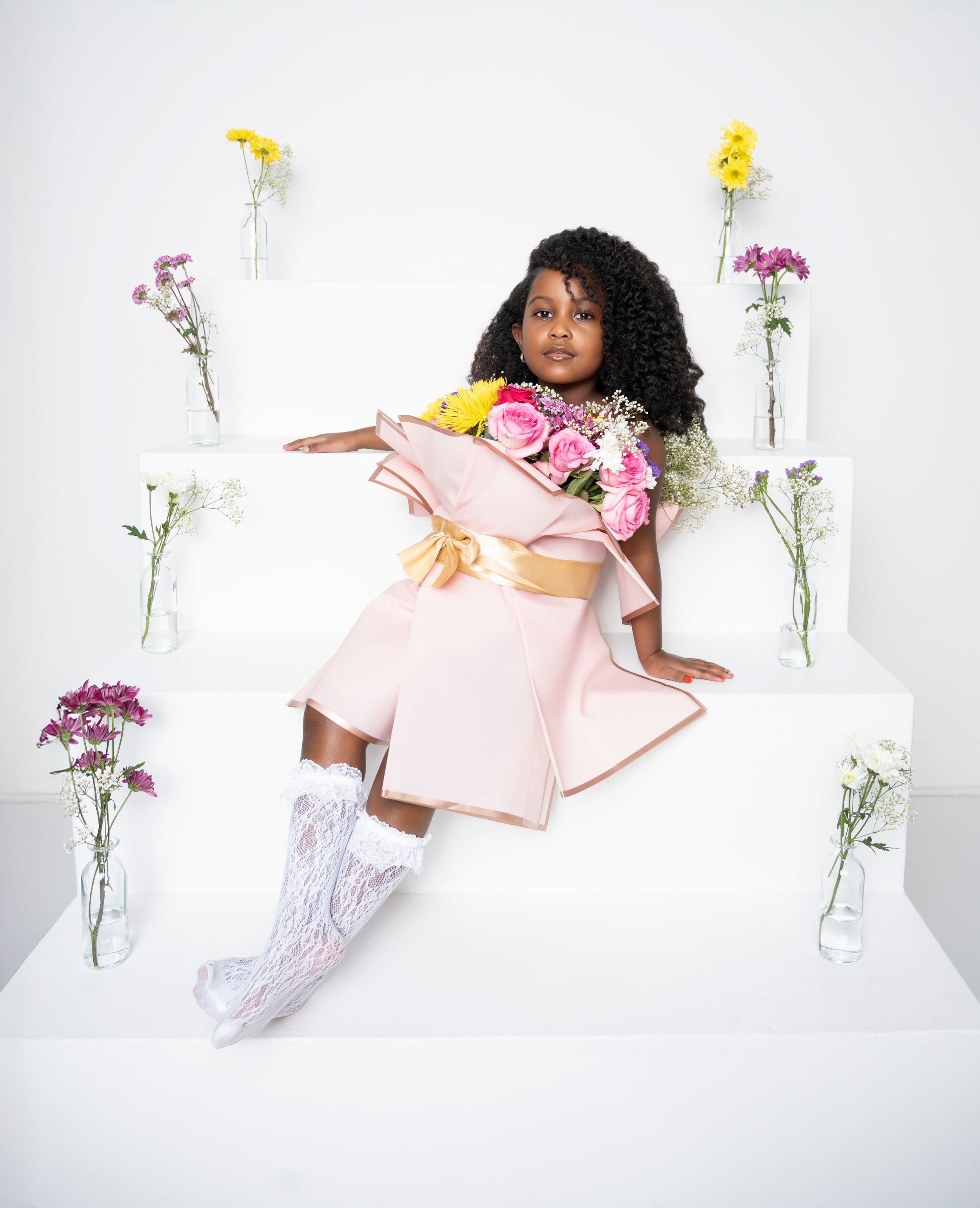 Artistic fashion photography series featuring a model in pink loungewear posing with delicate flowers in glass vases.
