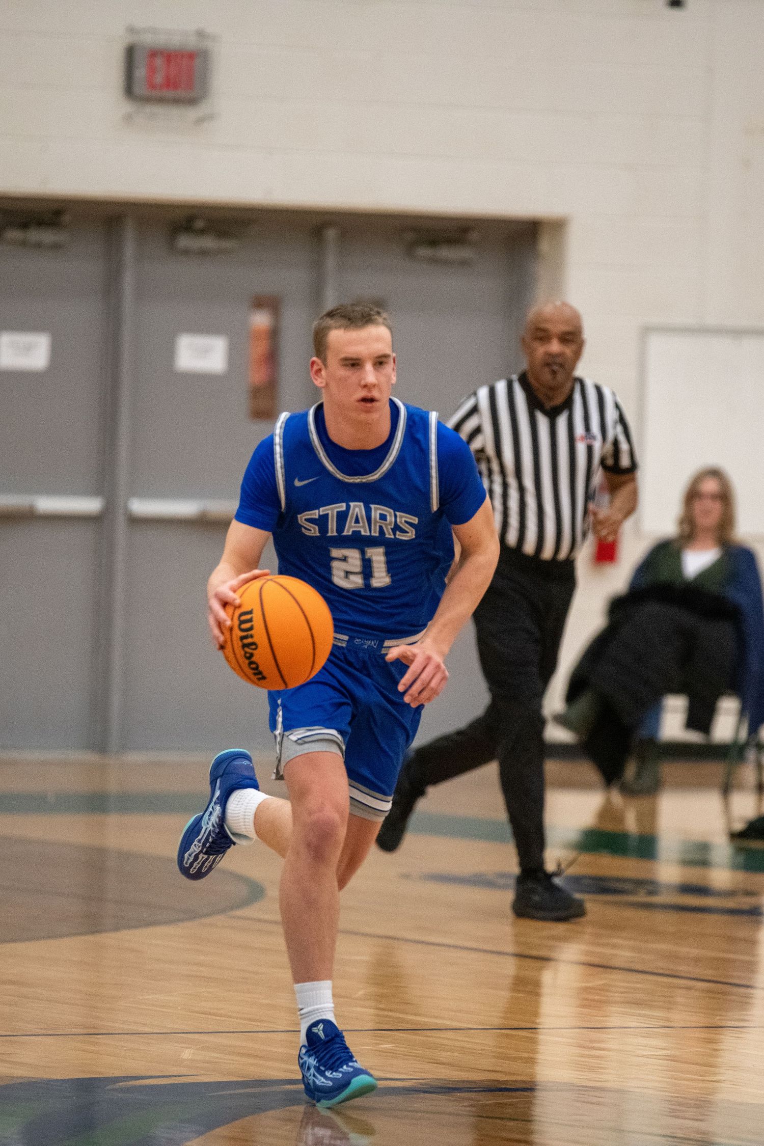 Basketball player in blue Stars jersey dribbles low while maintaining balance during an indoor game.