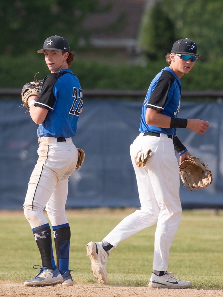 Two baseball players in blue uniforms stand back-to-back on the pitcher's mound.