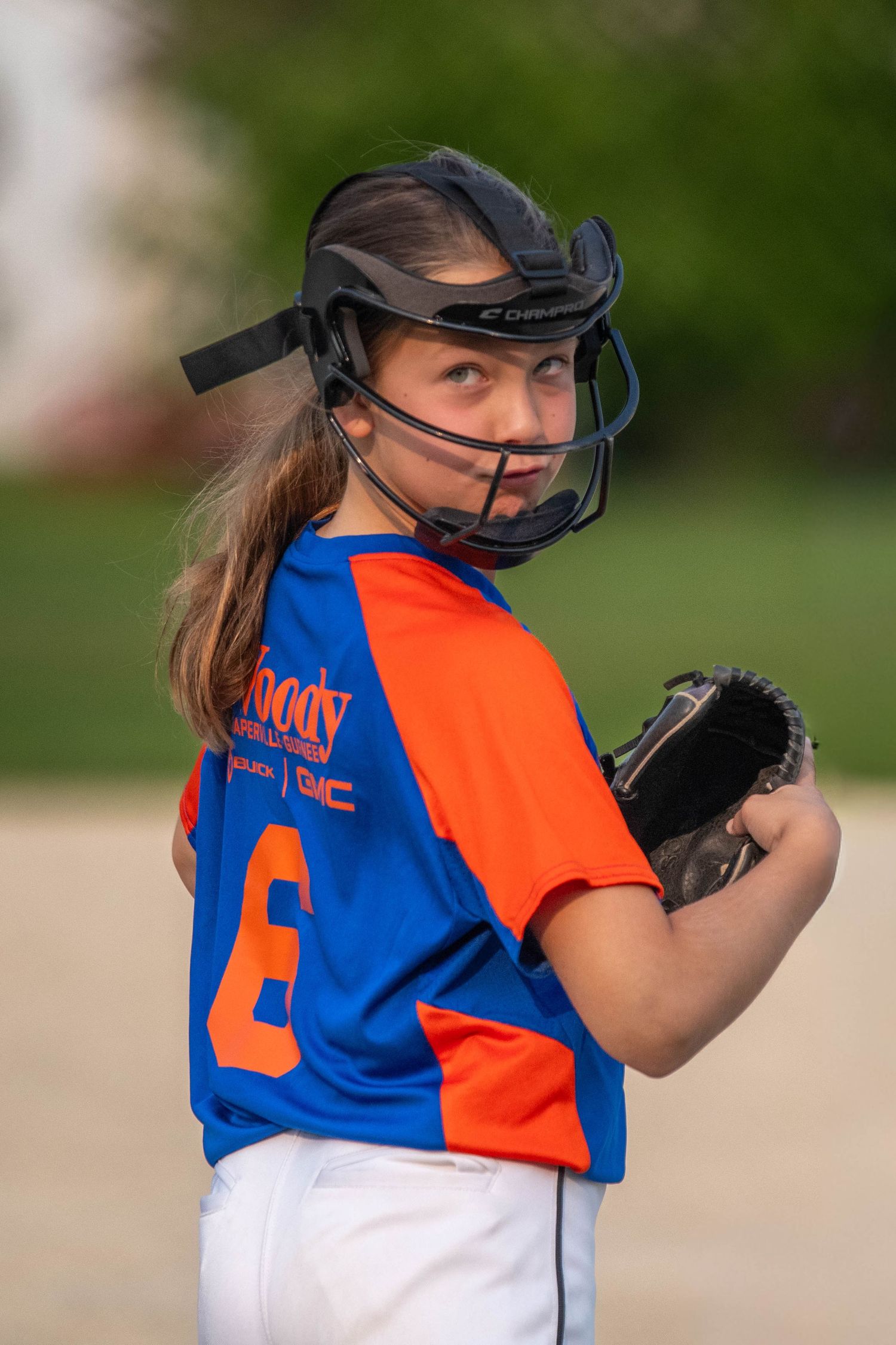A softball player in orange and blue uniform stands ready at bat during a game on a sunny day.