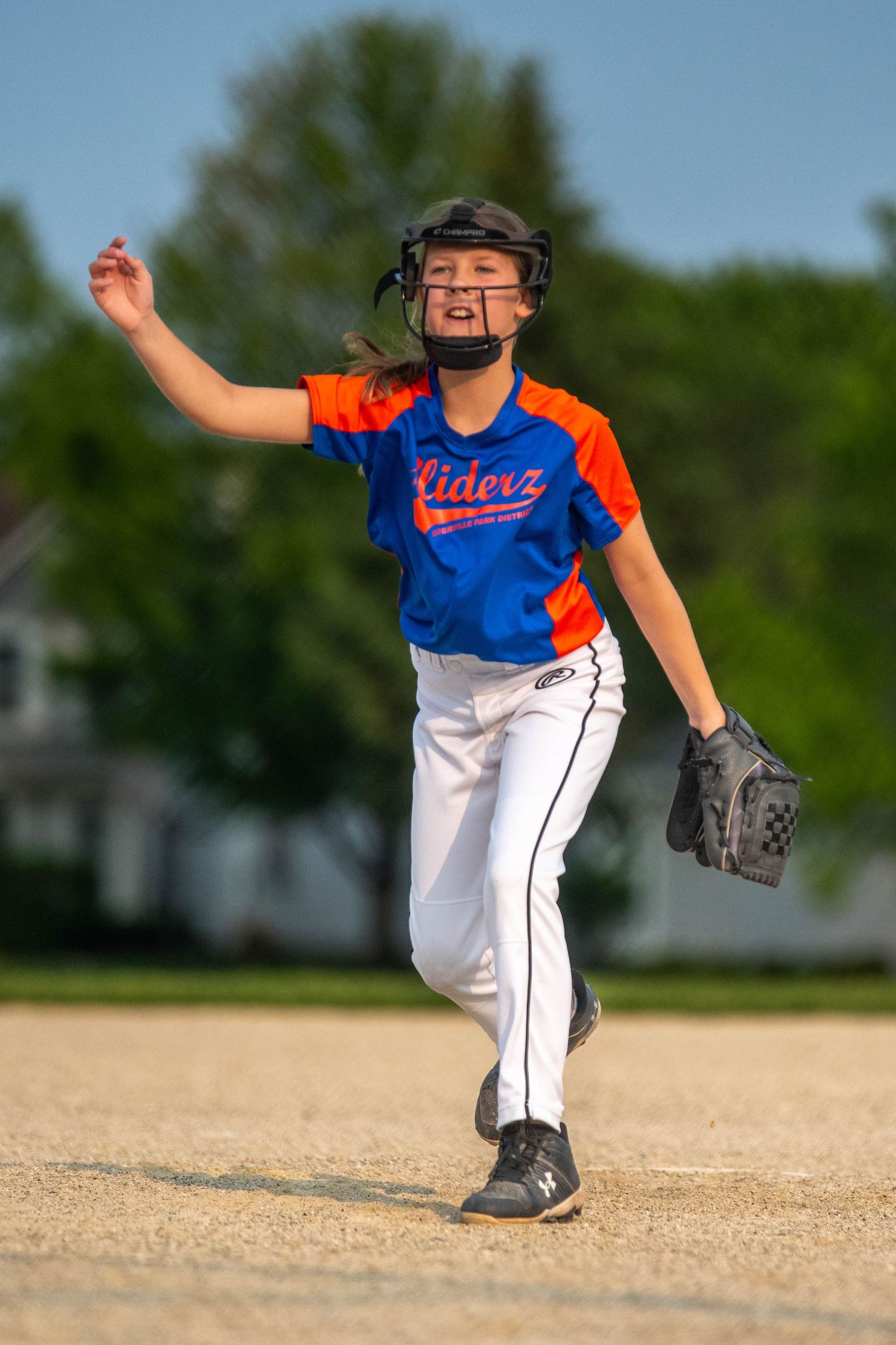 Youth baseball player in blue and orange uniform demonstrates pitching motion sequence on dirt infield.
