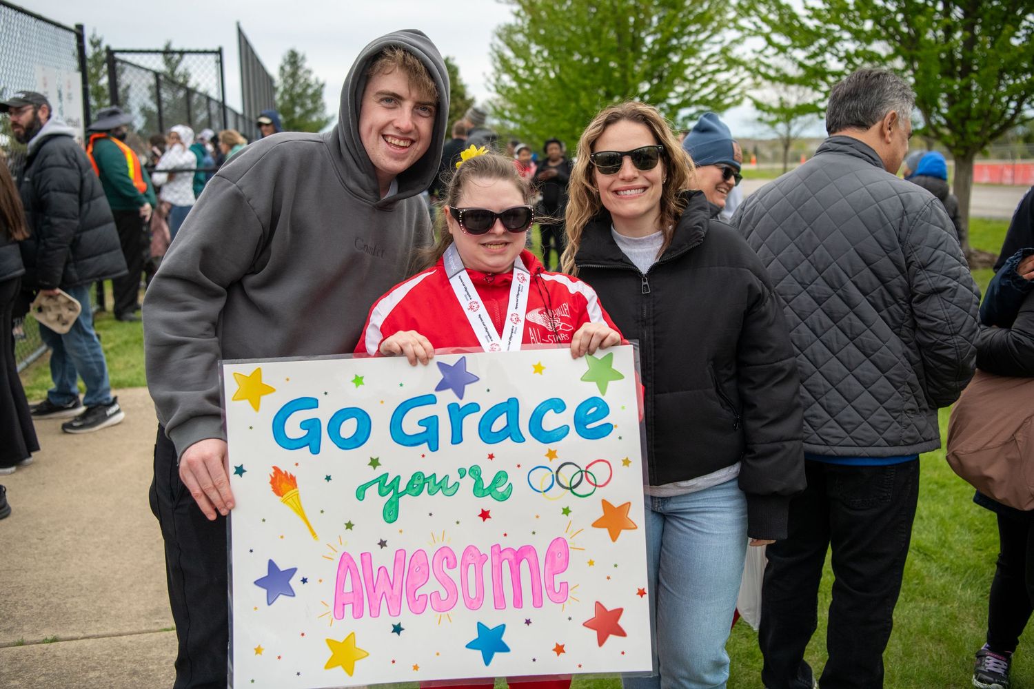 Supporters holding colorful encouraging signs at outdoor Special Olympics event.
