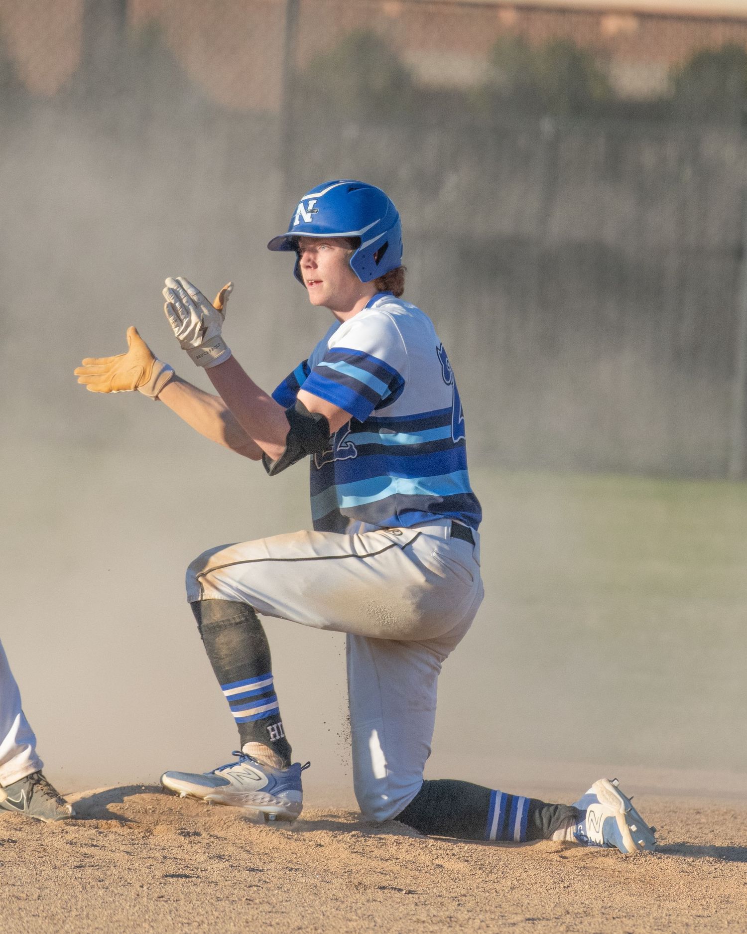 Baseball player in blue and white uniform kneels on dusty field during game.