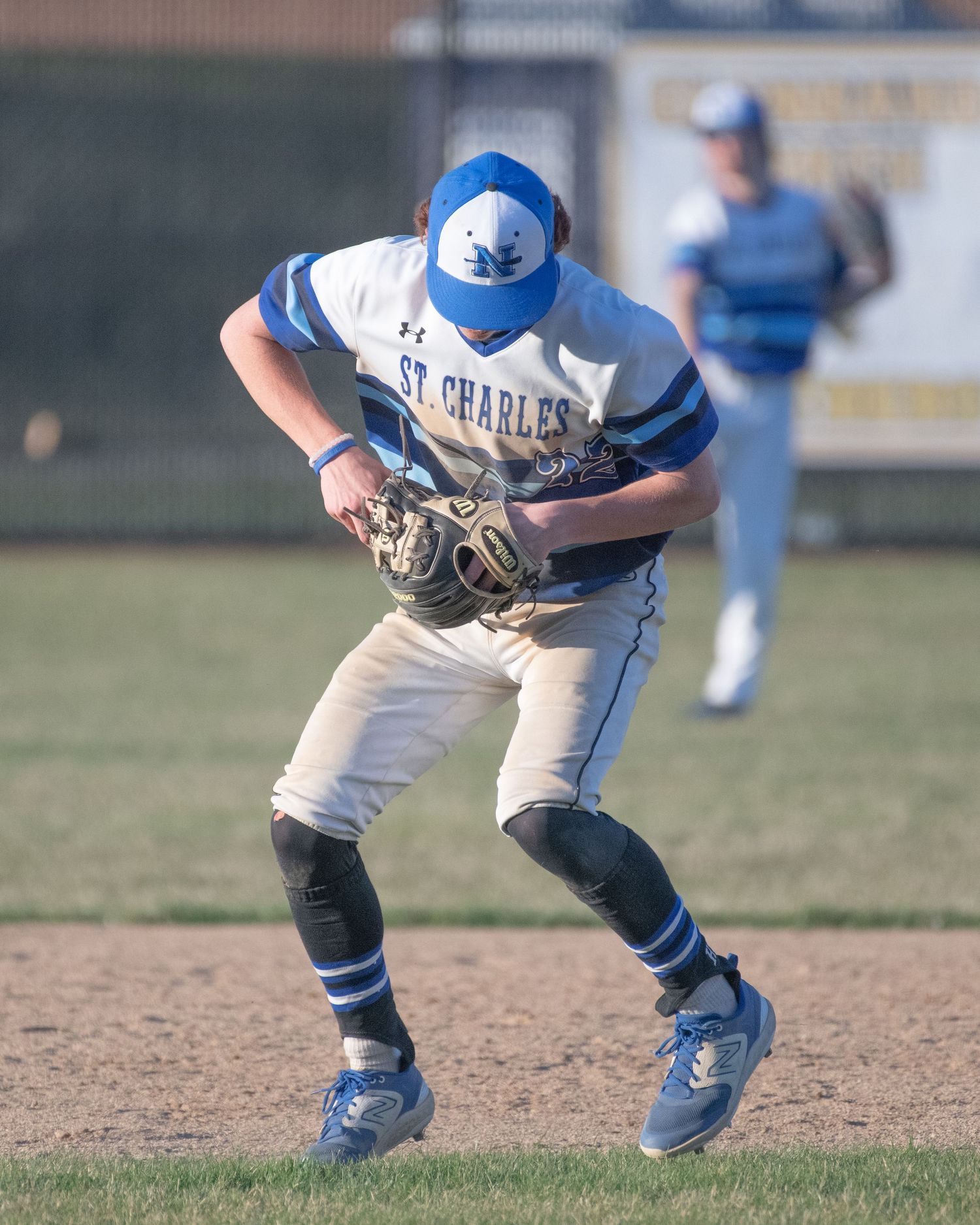 Baseball player in blue and white uniform fields a ground ball during a game.