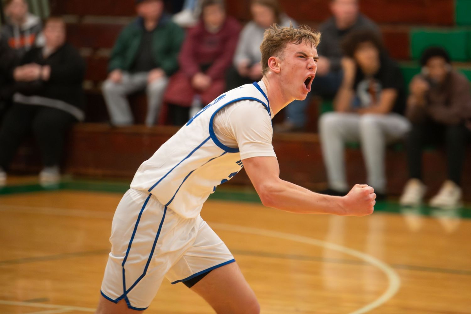 Basketball player in white and blue uniform leaps high to make a slam dunk during an intense game.