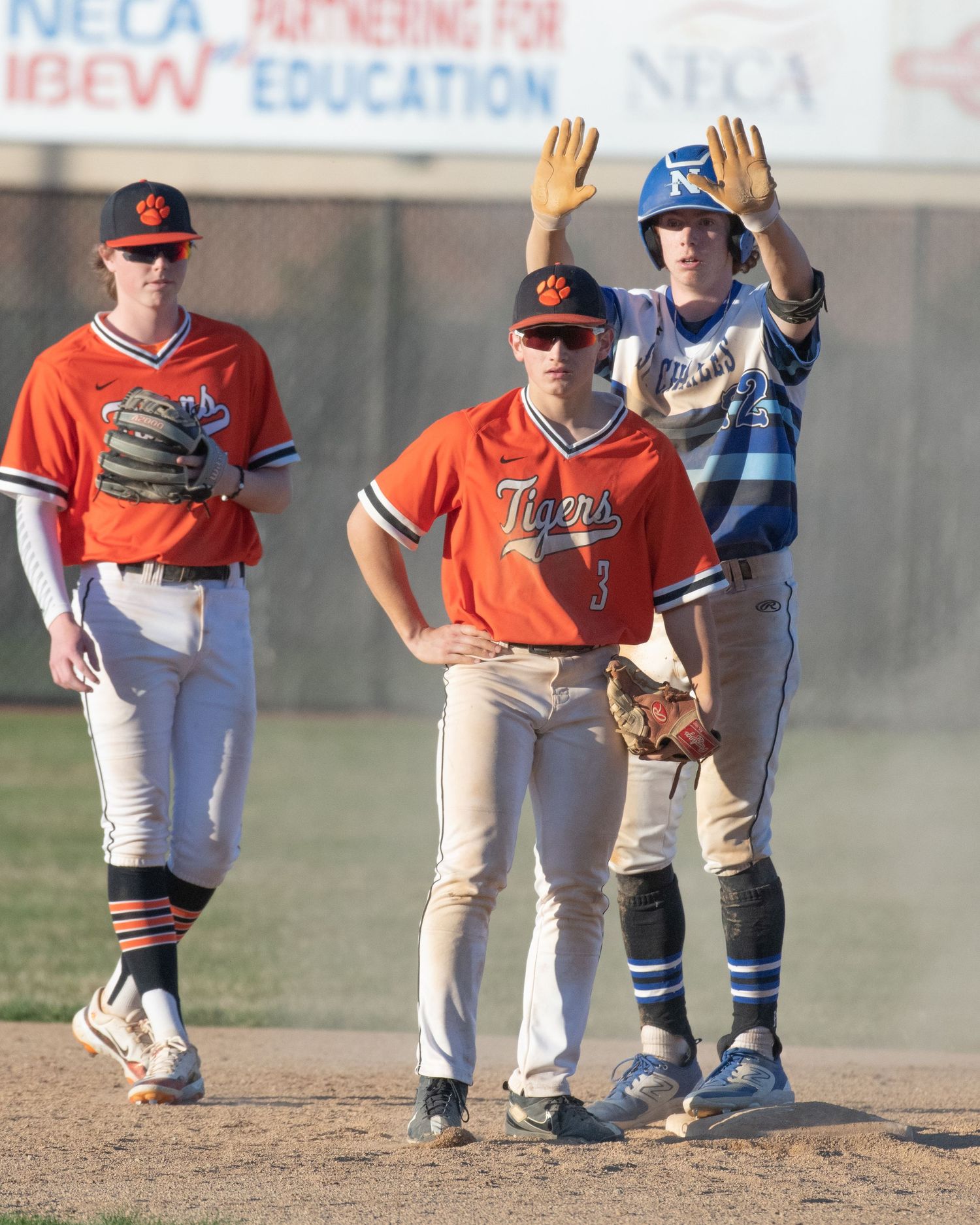 Baseball players from opposing teams in orange and blue uniforms stand on the baseball field during a game.