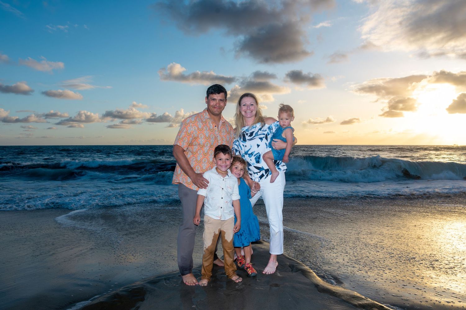San Diego family portrait photography of a family of five posing on a beach at sunset with ocean waves.