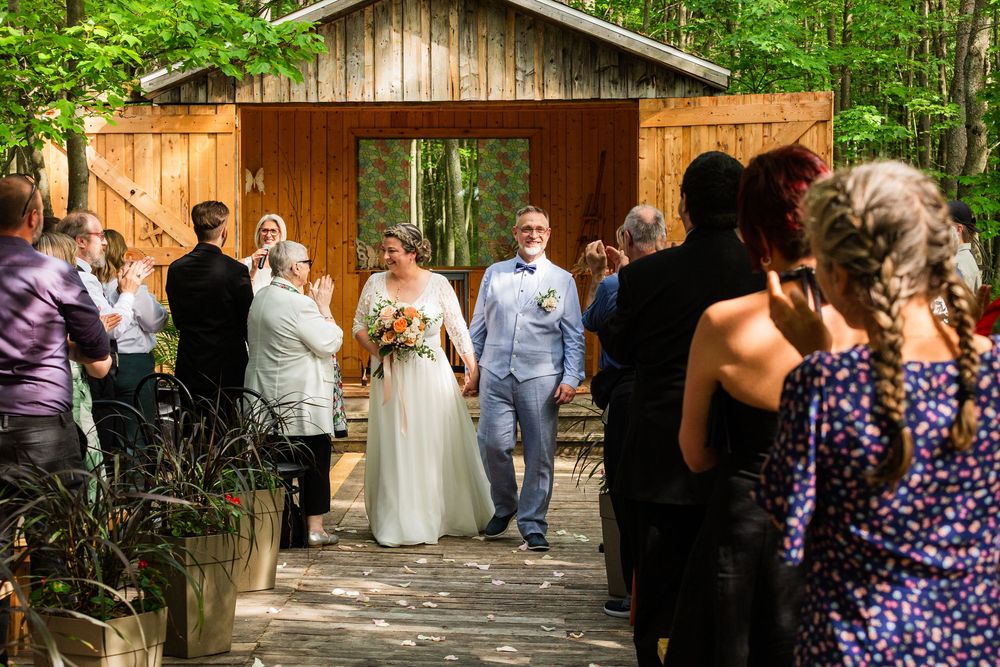 An outdoor wedding celebration on a wooden bridge surrounded by lush green forest and guests.