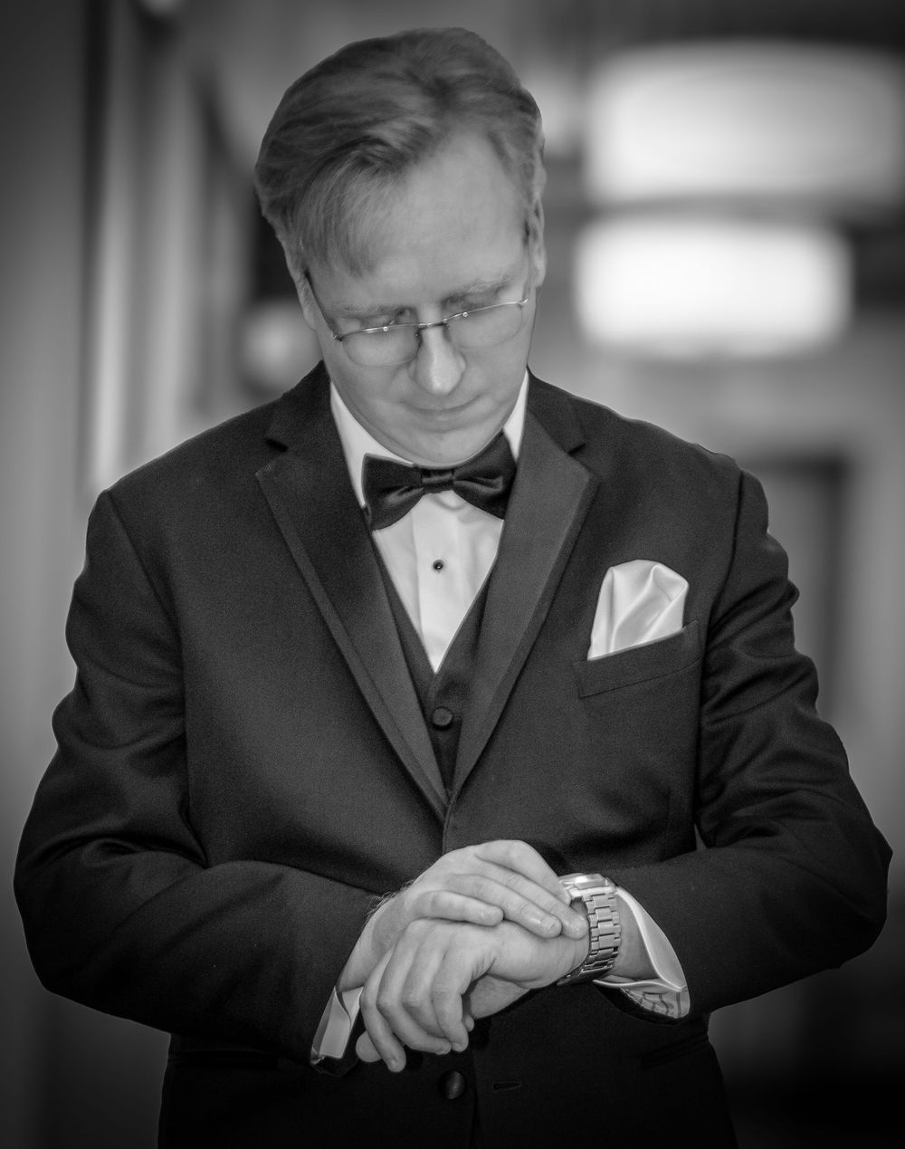 Formal portrait of person checking time on wristwatch while wearing classic black tuxedo.
