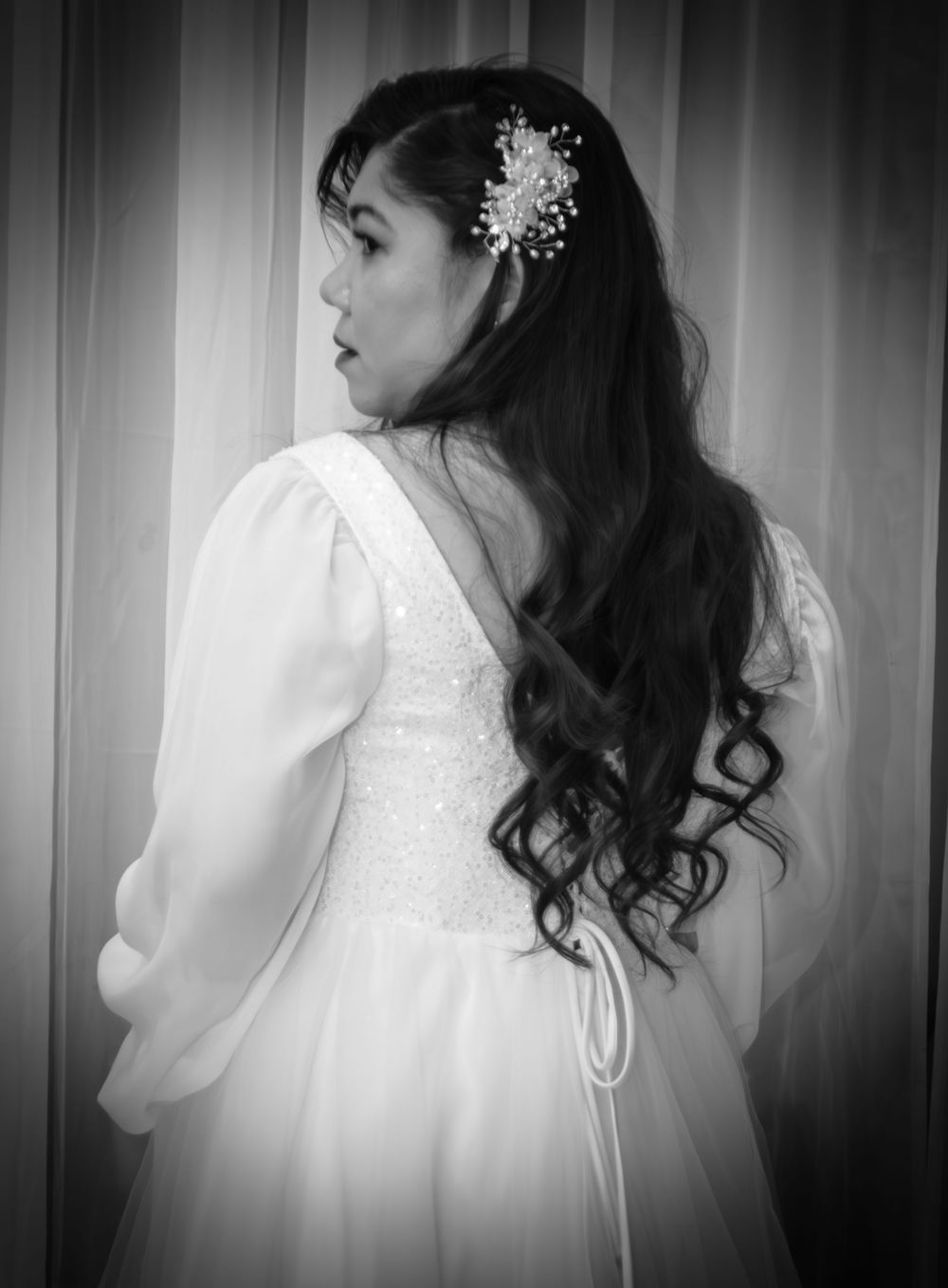 Side profile of bride in white gown with flowing curls and crystal hair accessory.
