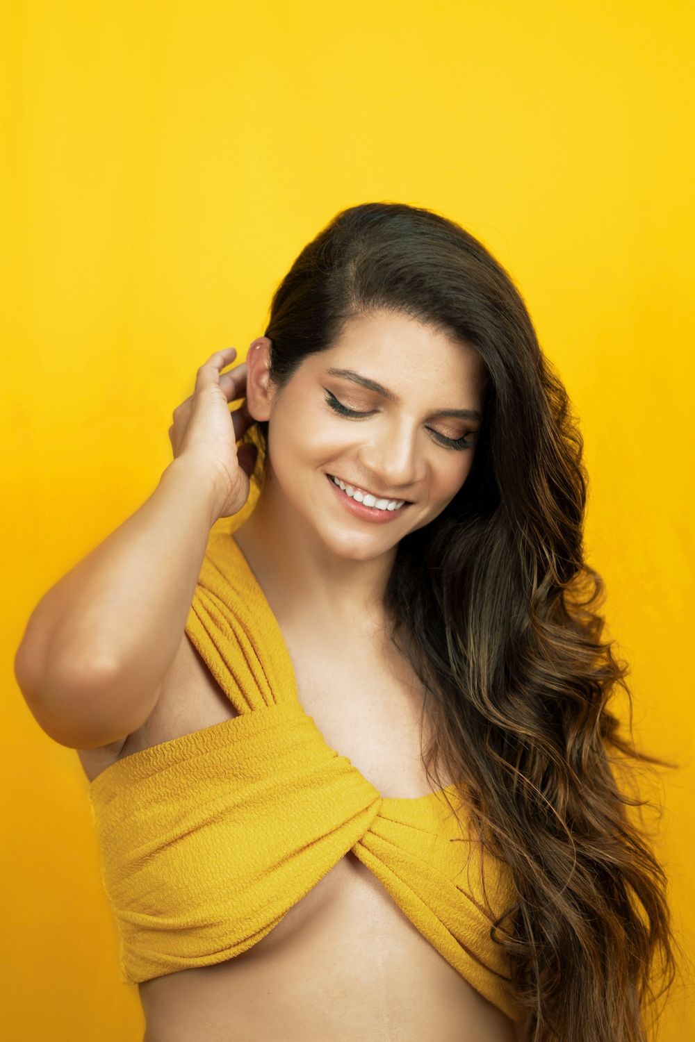 Fashion portrait against vibrant yellow background showing long wavy hair and yellow crop top.
