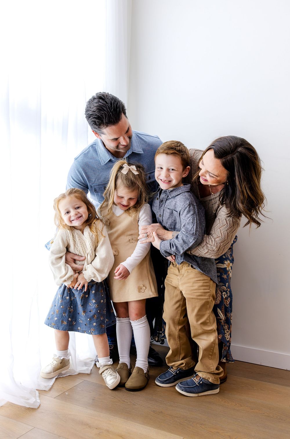 A family shares joyful moments together in a minimalist indoor setting with white walls and wooden floors.