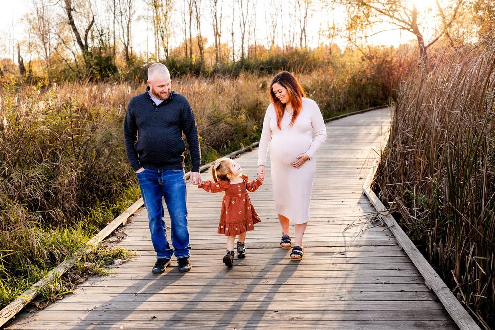 A wooden boardwalk path winds through autumn wetlands at sunset as people walk along it.